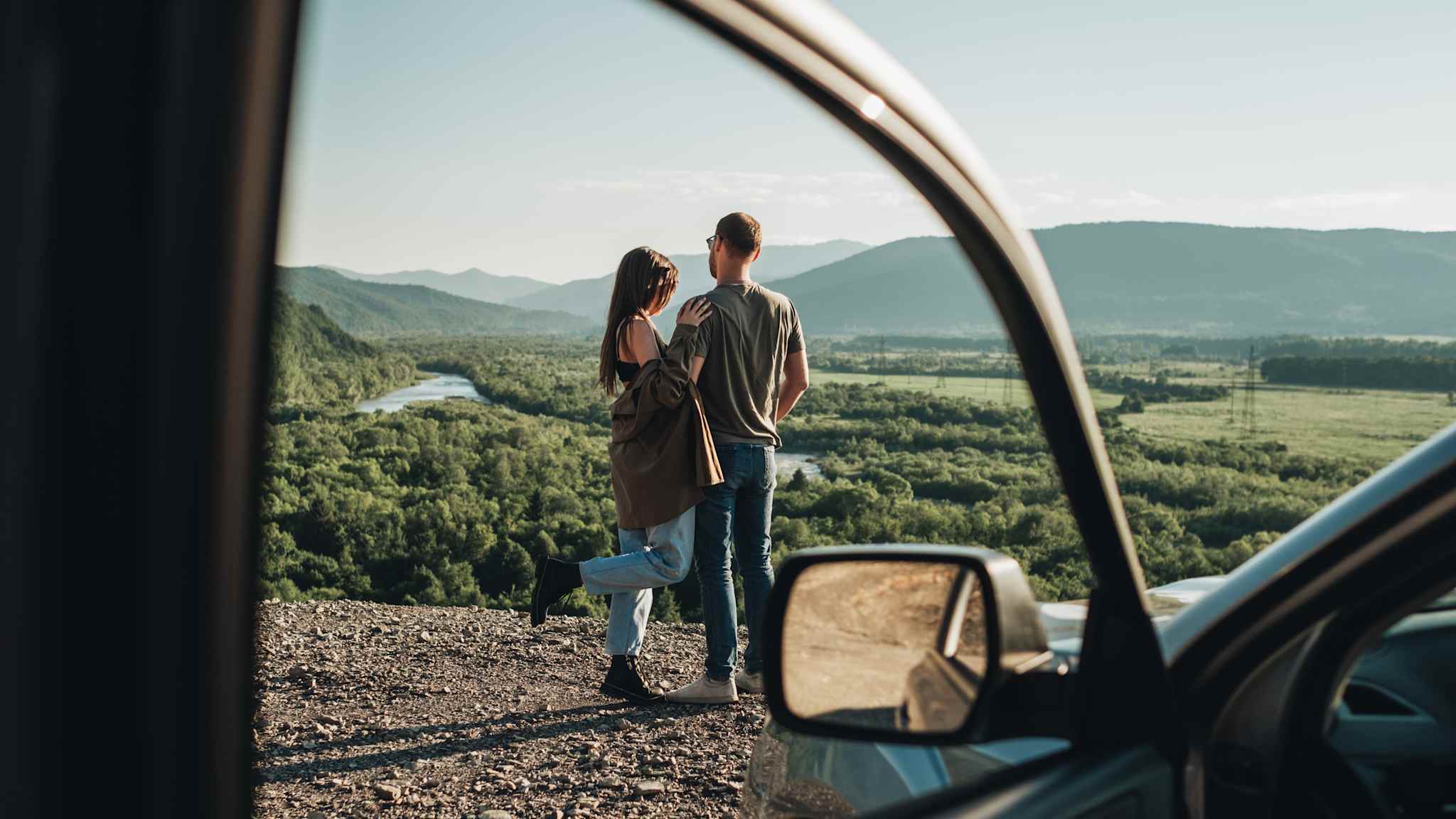 Ein Paar steht vor dem Auto an einem Aussichtspunkt. (c) 2020 Romvy/Shutterstock.